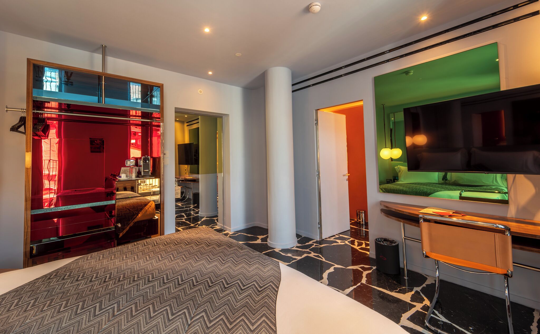 Una habitación de hotel moderna con cama, escritorio, televisor y espejo.