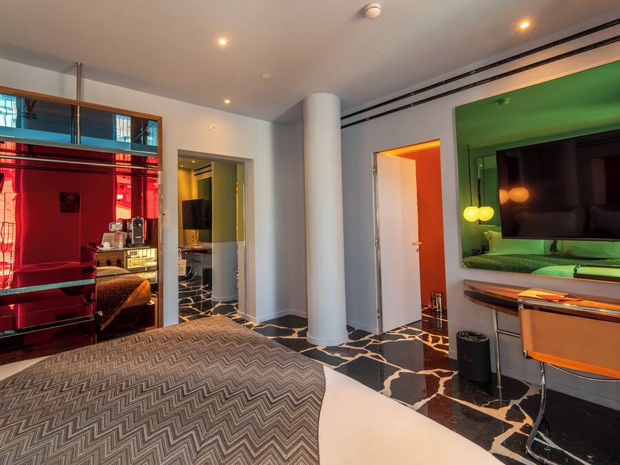 A modern hotel room with a bed, a desk, a TV, and a mirror.