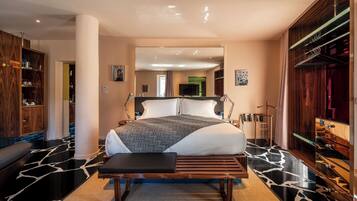 A modern bedroom with a large bed, a bench, a wardrobe, and a mirror.