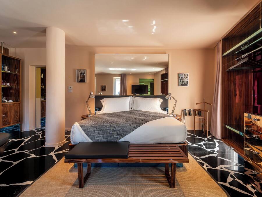 Un dormitorio moderno con una cama grande, un banco, un armario y un espejo.