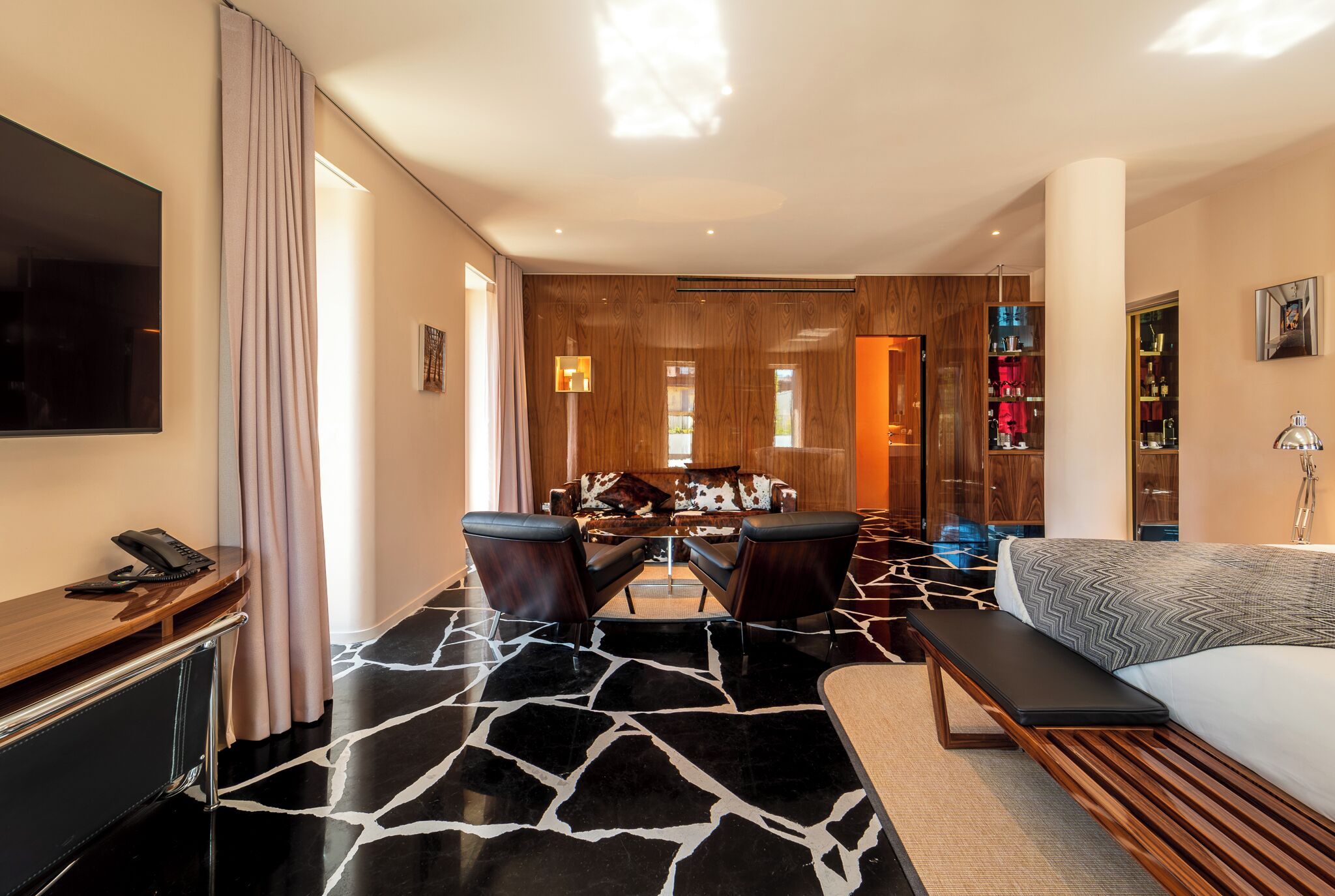 Una habitación de hotel moderna con una cama grande, un escritorio con teléfono, una zona de estar con sillas, una mesa de comedor y una estantería.