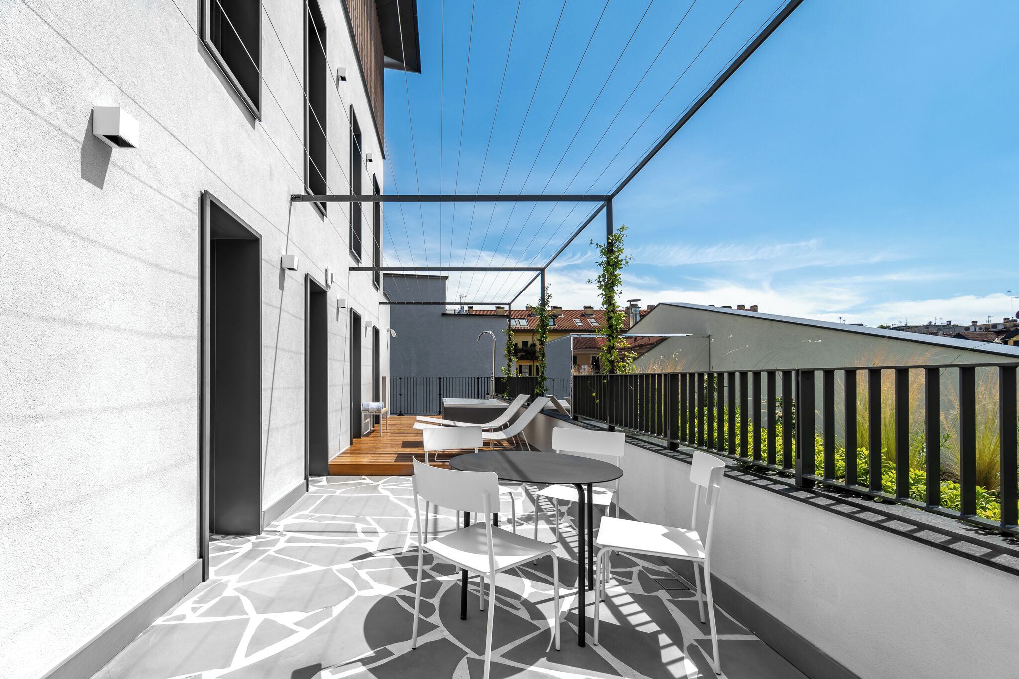 A modern outdoor patio with a dining area, a wooden deck, and a view of neighboring buildings.