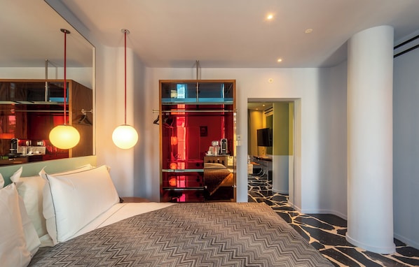 A modern hotel room with a large bed, a walk-in closet, a mirror, and a hallway leading to a bathroom. - Hotel Calimala Milano (Milan)
