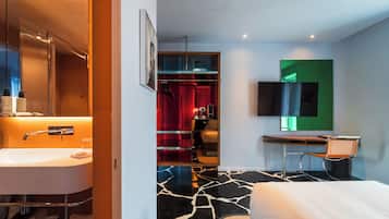 Habitación de hotel moderna con un baño amplio, una cama, un escritorio y un televisor.