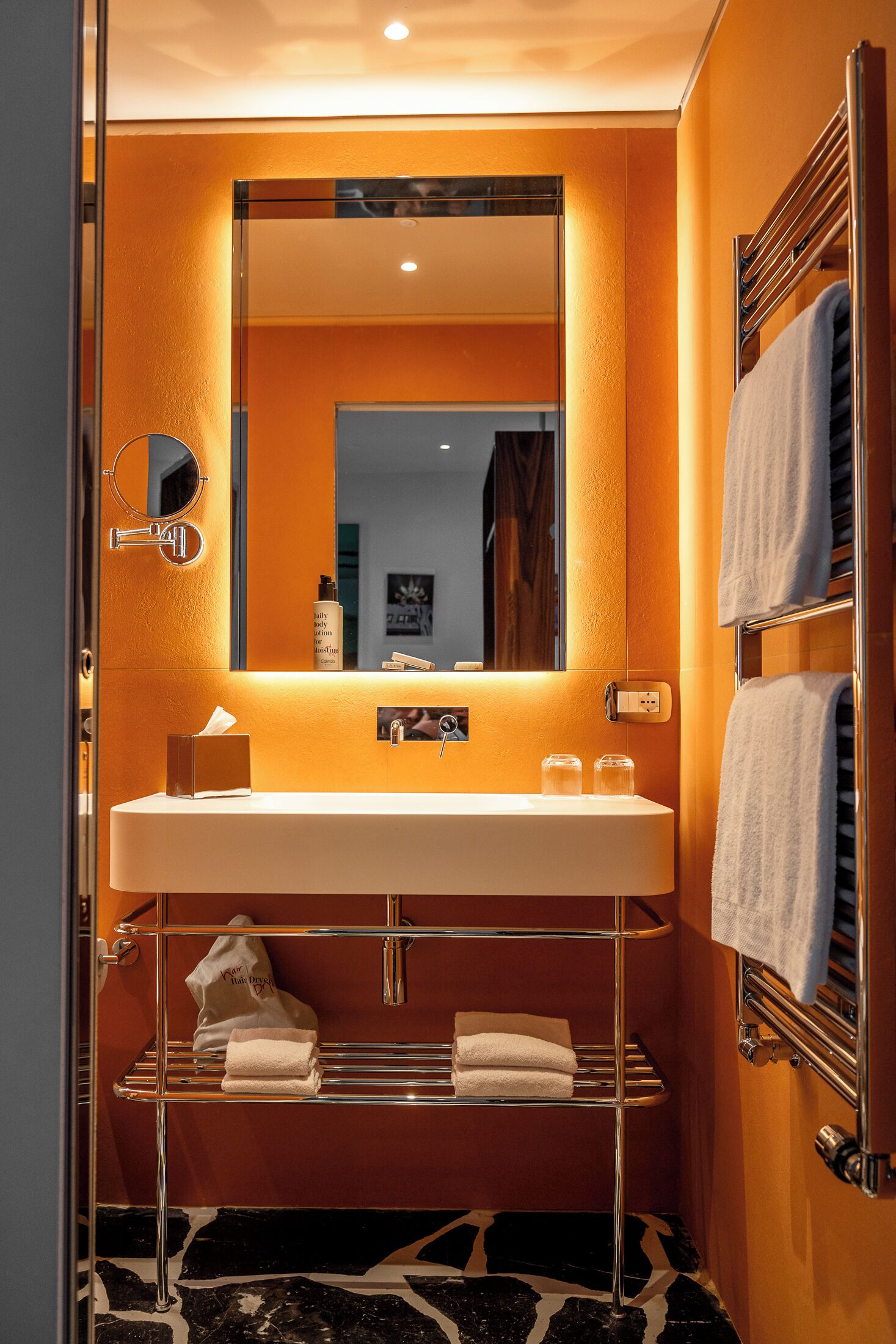 A bathroom with a white sink, a mirror, a towel rack, and a shelf with towels.
