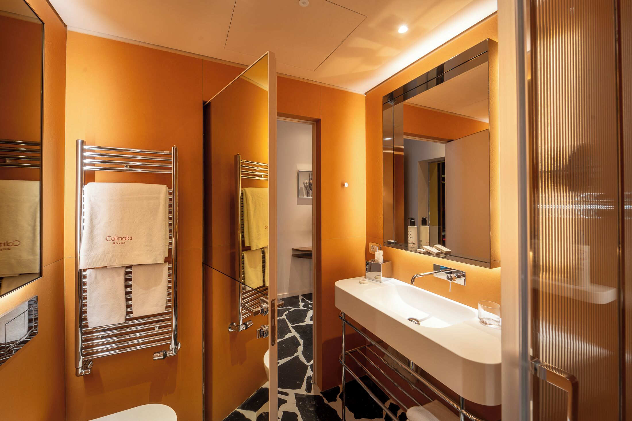 A modern bathroom with a large mirror, a white sink, and a towel rack with a white towel.