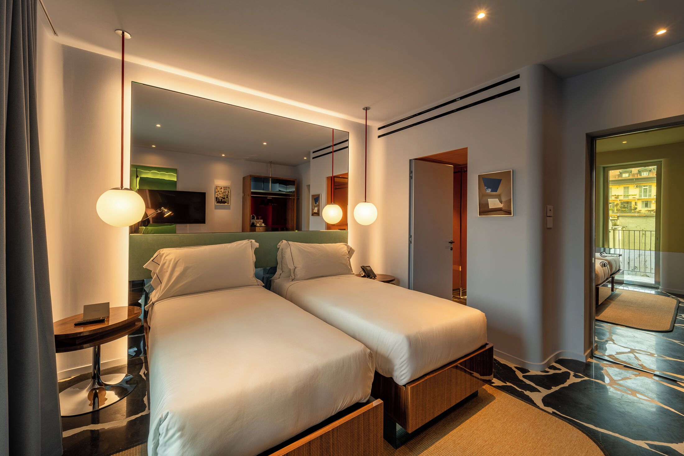 Een moderne hotelkamer met twee bedden, een flatscreen televisie, een klein tafeltje en een spiegel.