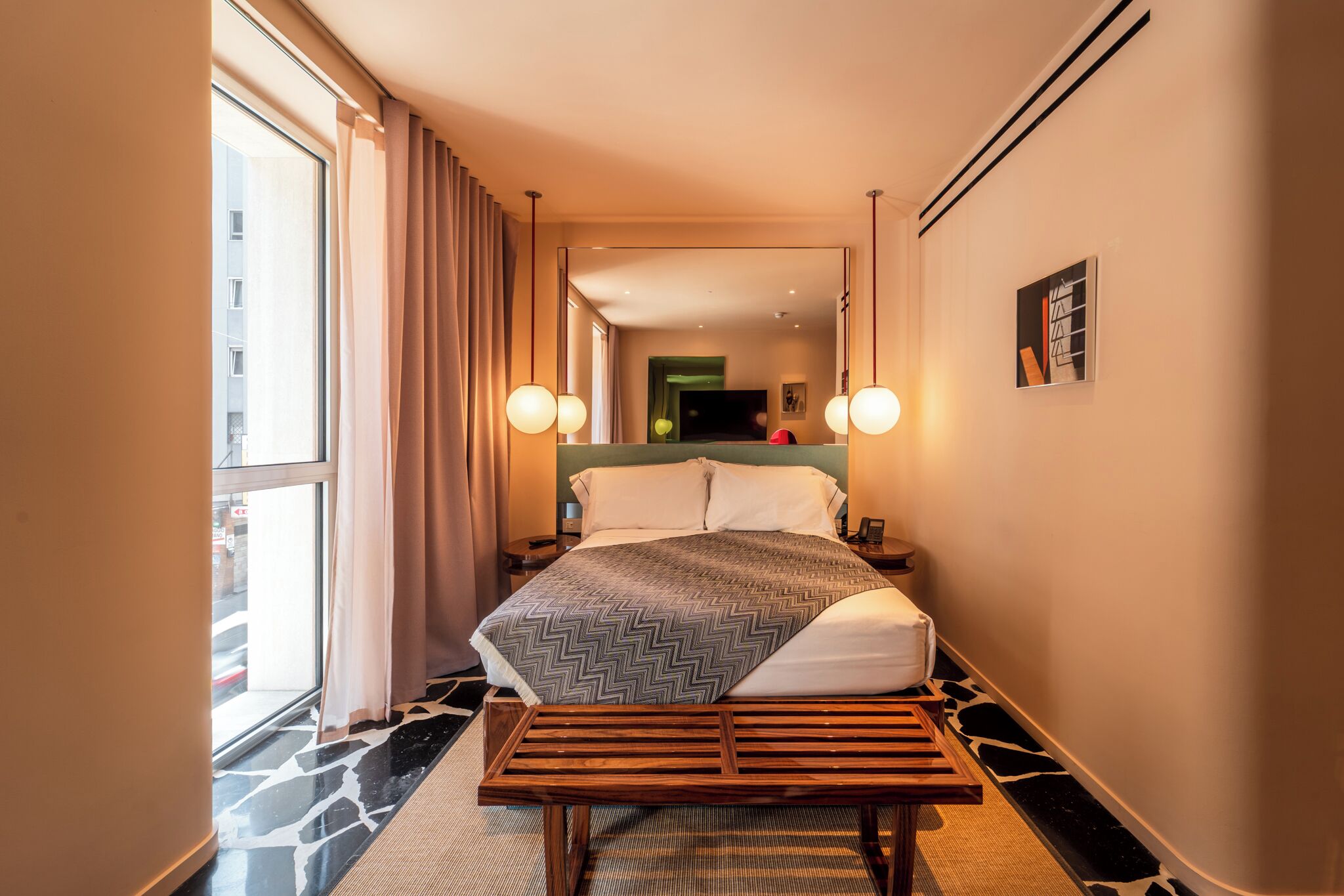 Ett hotellrum med en stor säng, en träbänk, en tv och en spegel.