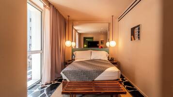 A hotel room with a large bed, a wooden bench, a TV, and a mirror.