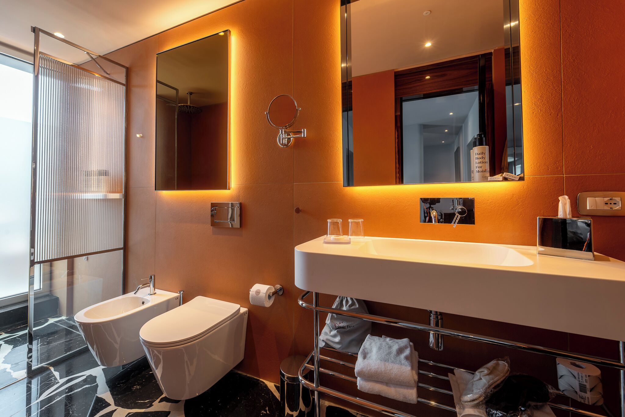 Un bagno moderno con uno specchio grande, due servizi igienici, un lavabo e un portasciugamani.