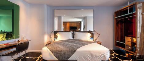 Una habitación de hotel moderna con una cama grande, un escritorio con una computadora portátil, un banco de madera y un espejo.