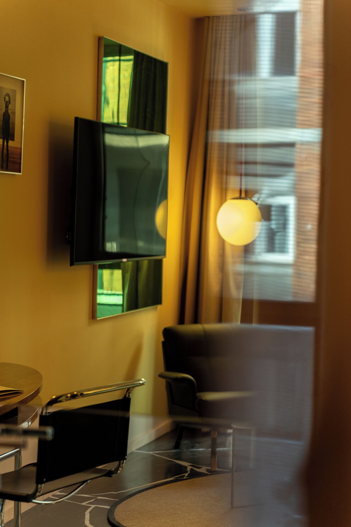 Una camera d'albergo moderna con televisione a schermo piatto montata a parete, una poltrona comoda, un tavolino e una finestra con tende.
