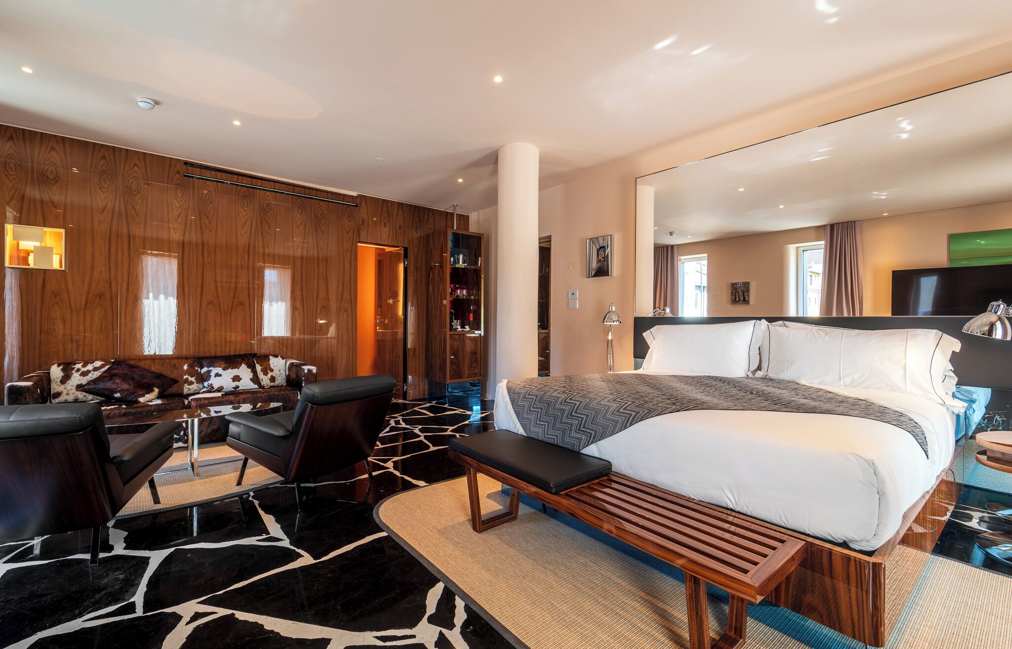 A modern hotel room with a large bed, a desk, and a sofa.