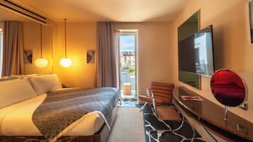 Quarto de hotel com cama, escrivaninha, cadeira, televisão e varanda com vista para edifícios.