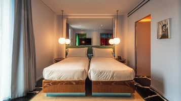 A double bed with a wooden frame and a mirror above it. There is a small bedside table with a lamp and a phone. The room has a black and white marble floor and a large window with curtains.