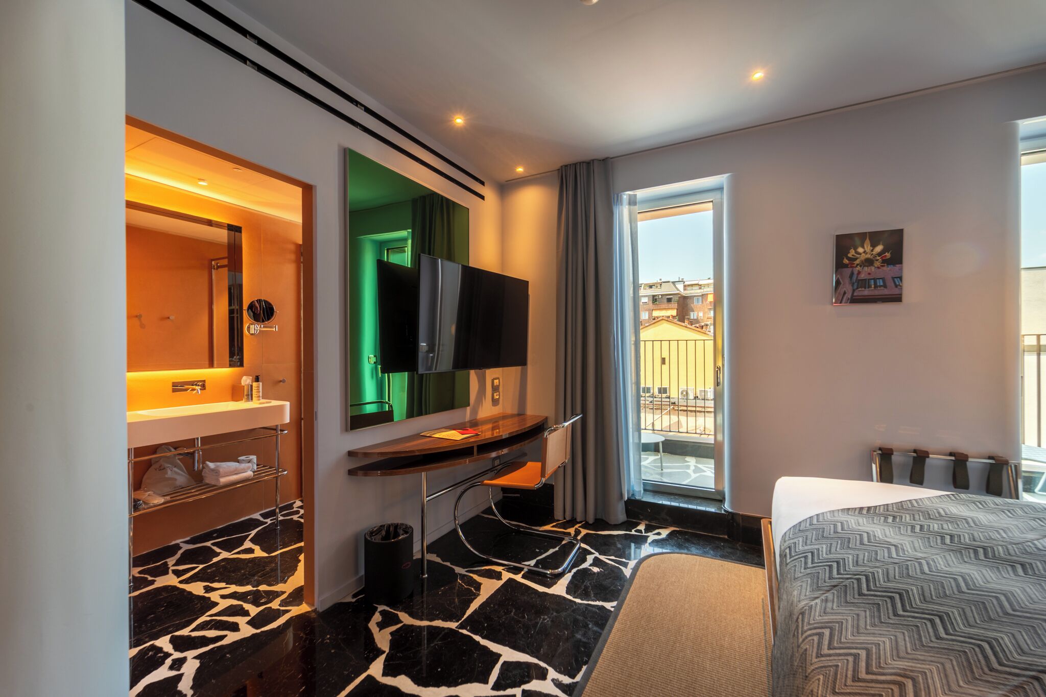 Una camera d'albergo con bagno, una scrivania, un letto e vista sulla città.