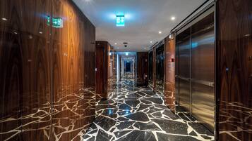 Een gang met gepolijste marmeren vloeren, houten lambrisering en een lift.