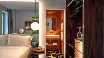 Habitación de hotel moderna con cama, una mesita redonda, un escritorio pequeño, baño con tocador y espejo.