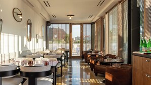 A modern hotel lobby with round tables, comfortable seating, and large windows offering a view of the city. - Hotel Calimala Milano (Milan)