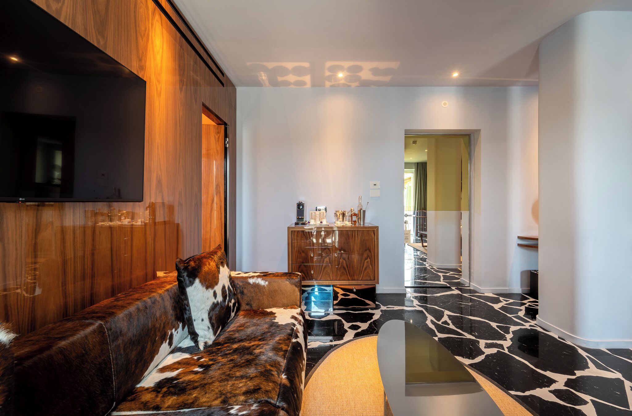 Un salón moderno con pared de madera, sofá de cuero, mesa de centro de cristal y suelo de mármol.