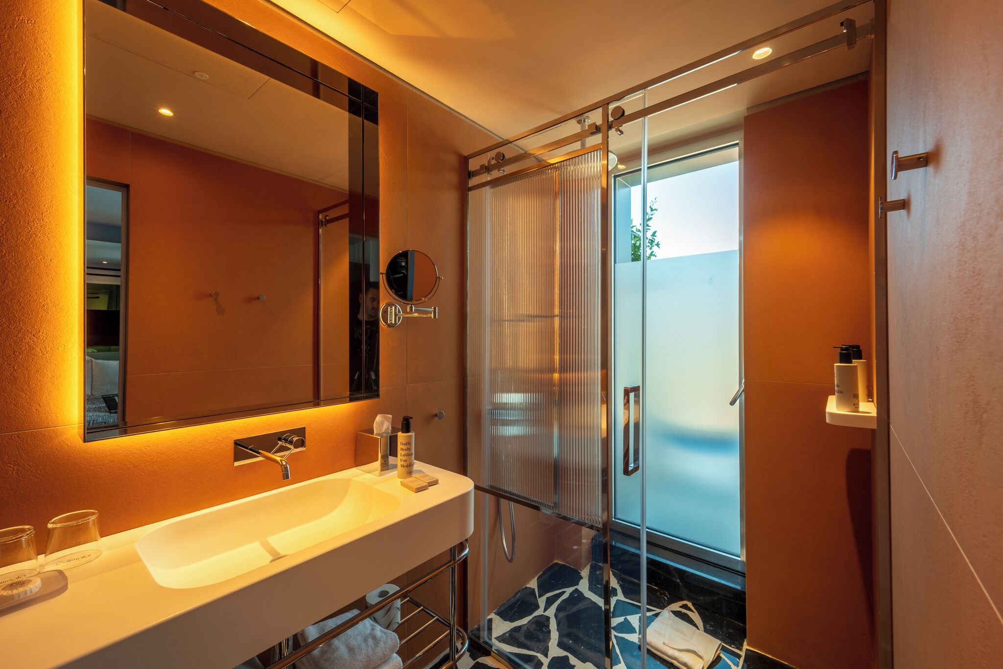 Un baño moderno con cabina de ducha de vidrio, un espejo grande y un lavamanos blanco.
