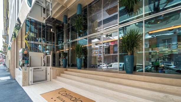 A modern building with large glass windows, a reception desk, and a doormat with the name "Calimala". - Hotel Calimala Milano (Milan)