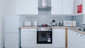 A compact kitchen with white cabinets, a stainless steel range, a built-in oven, a microwave, and a coffee maker. - Stunning Home, Ideal for Business, FREE Parking! (Greater Manchester)