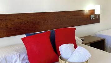 Une chambre d’hôtel avec un lit, des oreillers rouges et blancs, un élément décoratif mural, une table de chevet avec une lampe et un panier contenant des serviettes.