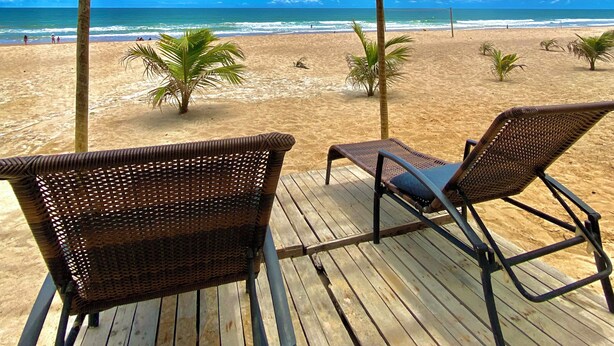 A wooden deck with wicker chairs overlooking a beach. - Imperial Arembepe Beach Hotel (Camaçari)