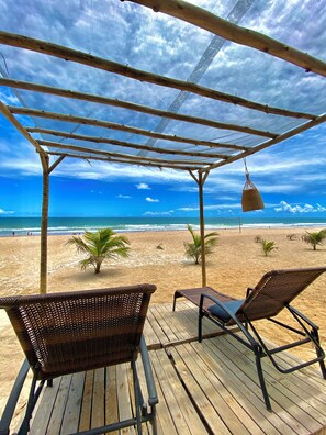 Una terraza de madera con sillas de mimbre que da a una playa.