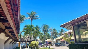 A pathway leading to a building with a tiled roof and a covered area with a glass wall. - Imperial Arembepe Beach Hotel (Camaçari)