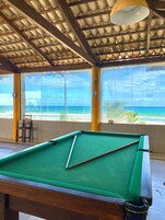 Una mesa de billar en una habitación con ventanas amplias que dan a la playa.