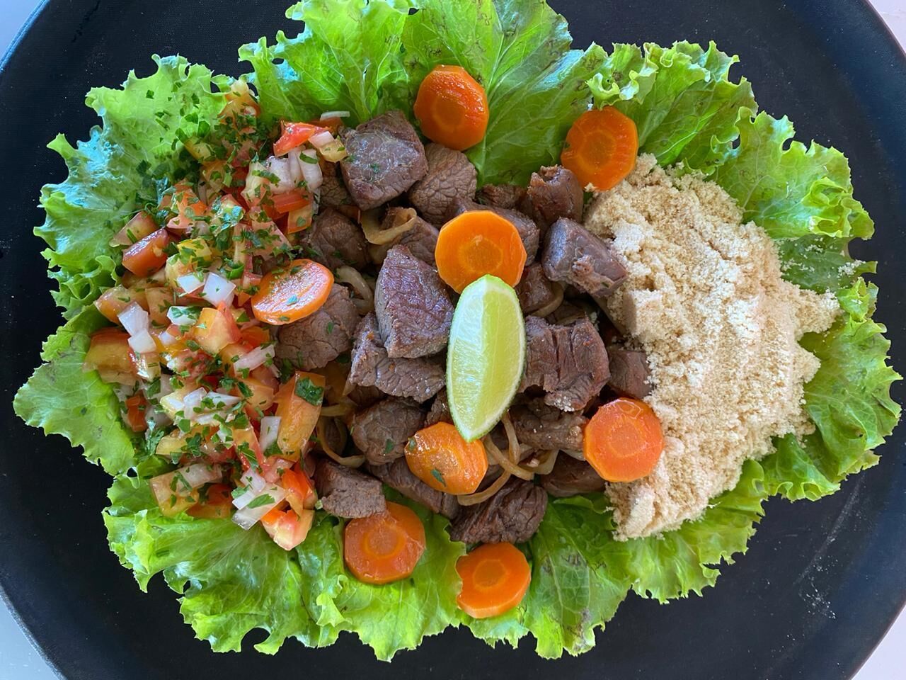 A plate of food with beef, carrots, and a lime wedge on lettuce leaves.
