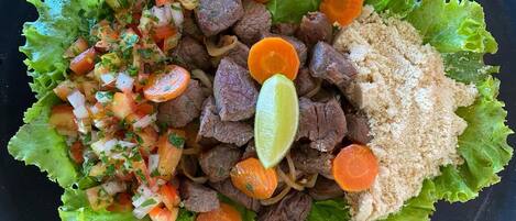 Un plato de comida con carne de res, zanahorias y una cuña de limón sobre hojas de lechuga.