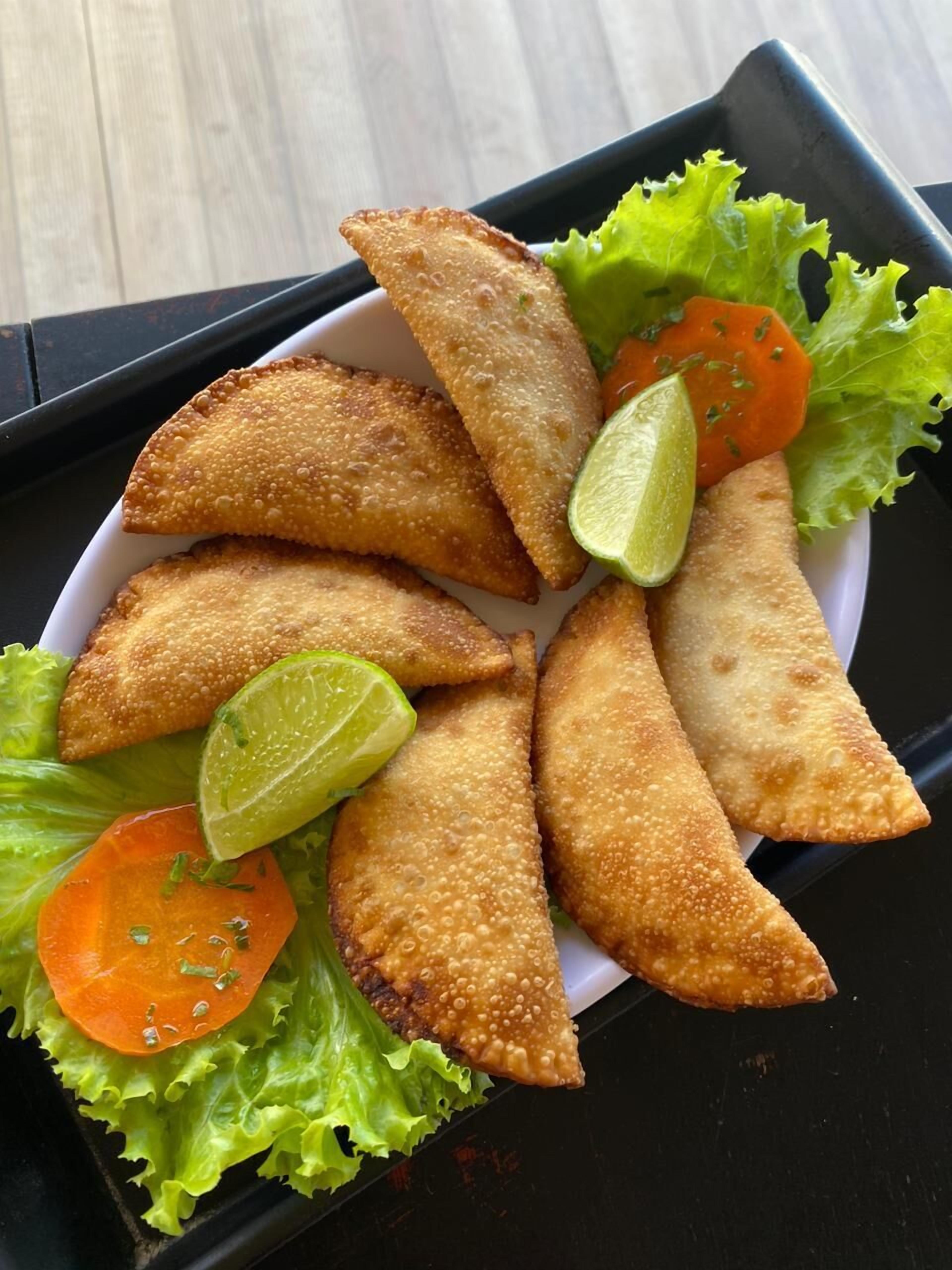 A plate of fried pastries with lime wedges and lettuce.
