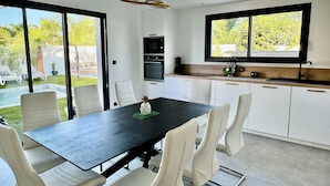 Una cocina moderna con armarios blancos, encimera negra y zona de comedor con mesa negra y sillas blancas.