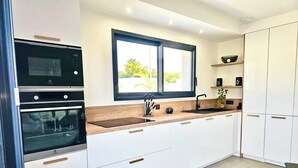 Una cocina moderna con armarios blancos, encimera de madera, horno integrado y ventana con vistas a la vegetación.