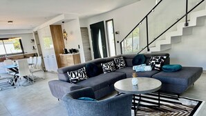 Una sala moderna con un sofá seccional gris, una mesa redonda de centro y una escalera que conduce a un nivel superior.