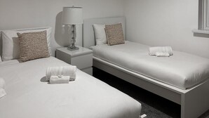 Quarto de hotel com duas camas, uma mesa de cabeceira e uma luminária, e uma janela.