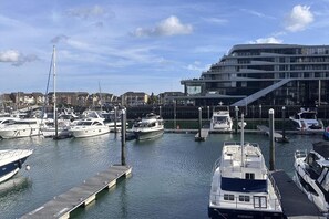 Un porto turistico con diverse imbarcazioni ormeggiate, un edificio moderno dalle facciate in vetro e un cielo sereno.