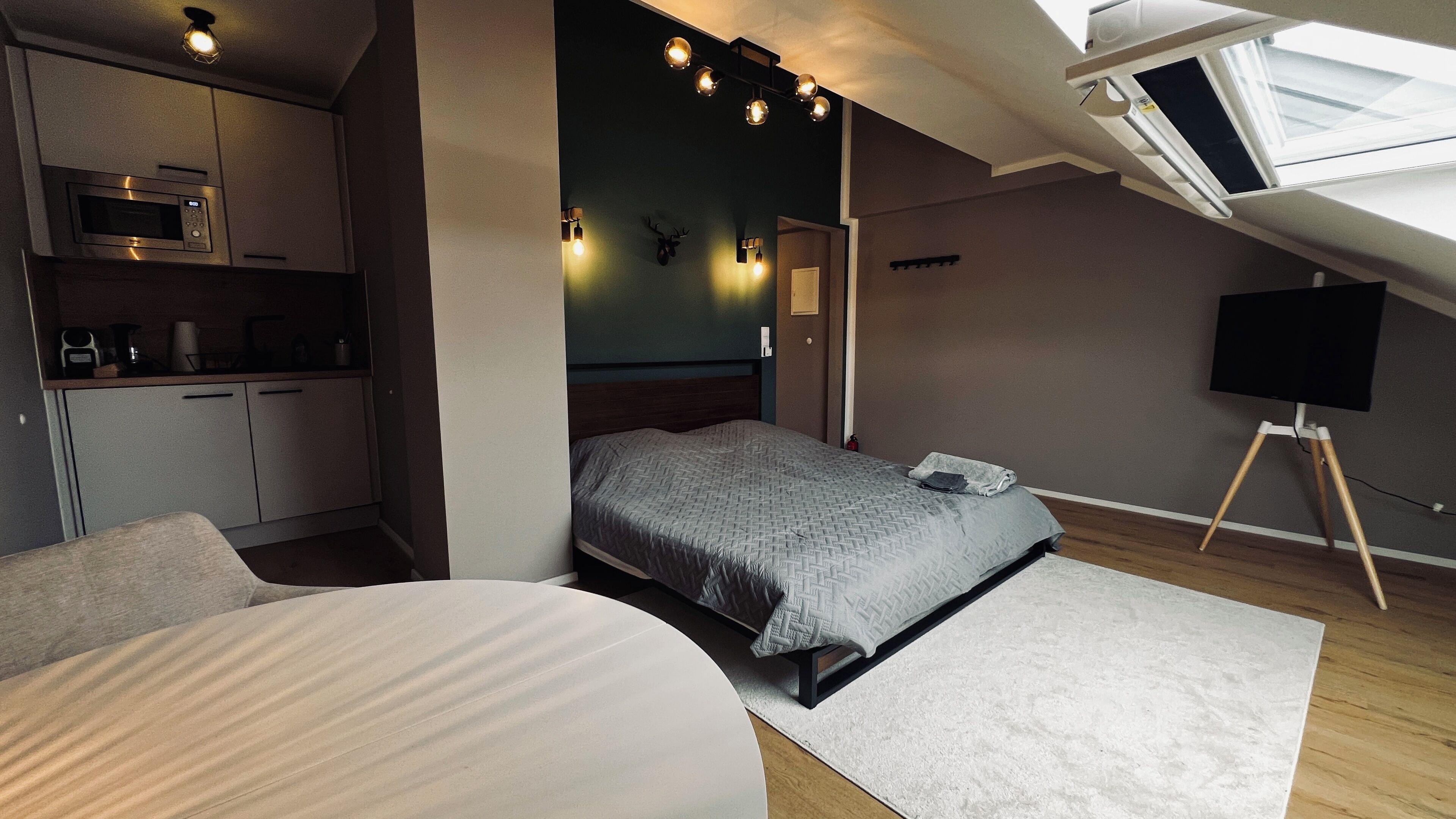 Een kleine slaapkamer met een bed, bureau en kitchenette.