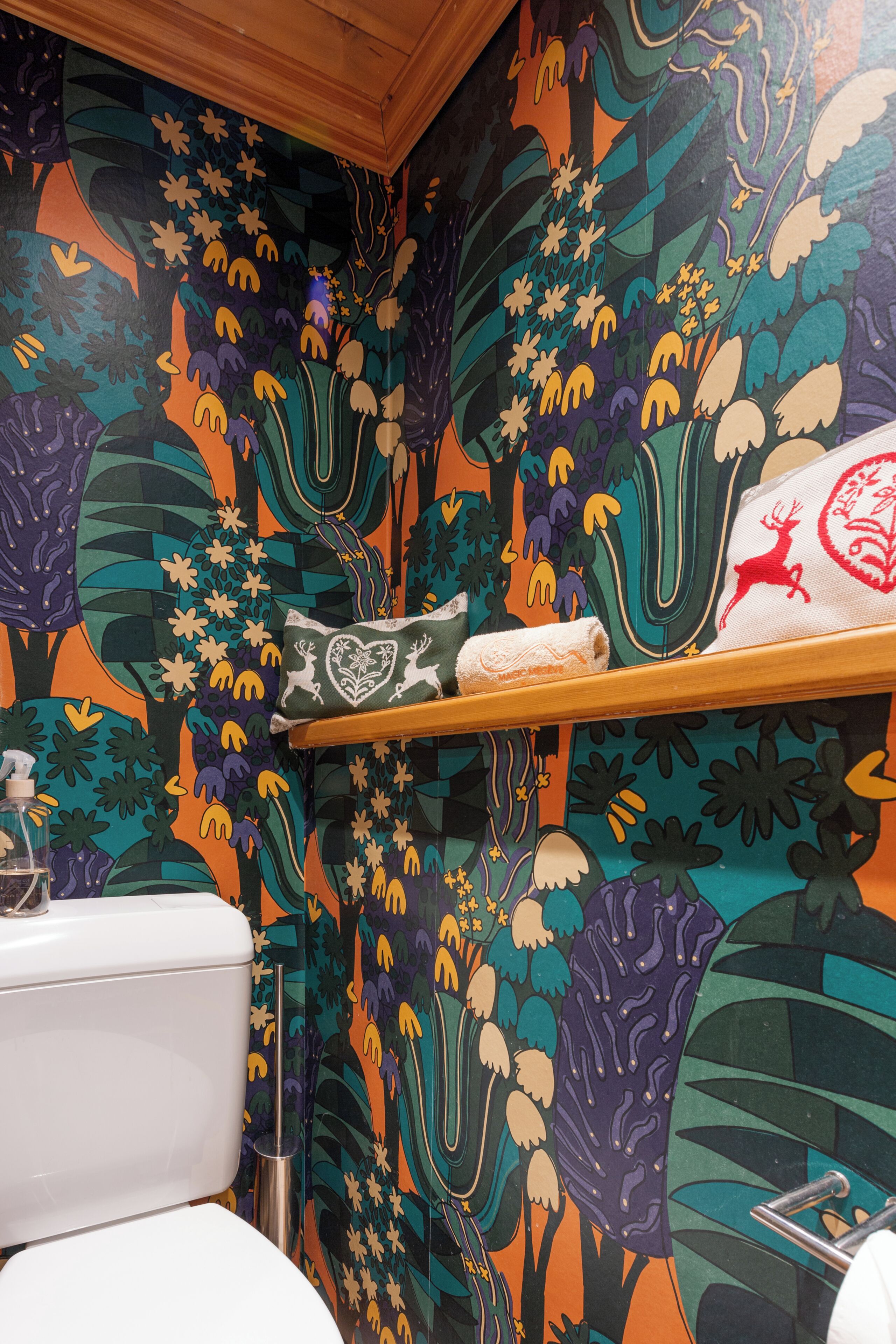A bathroom with a colorful floral wallpaper, a white toilet, and a shelf with a towel and a decorative item.
