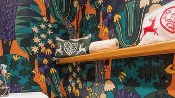 A bathroom with a colorful floral wallpaper, a white toilet, and a shelf with a towel and a decorative item.