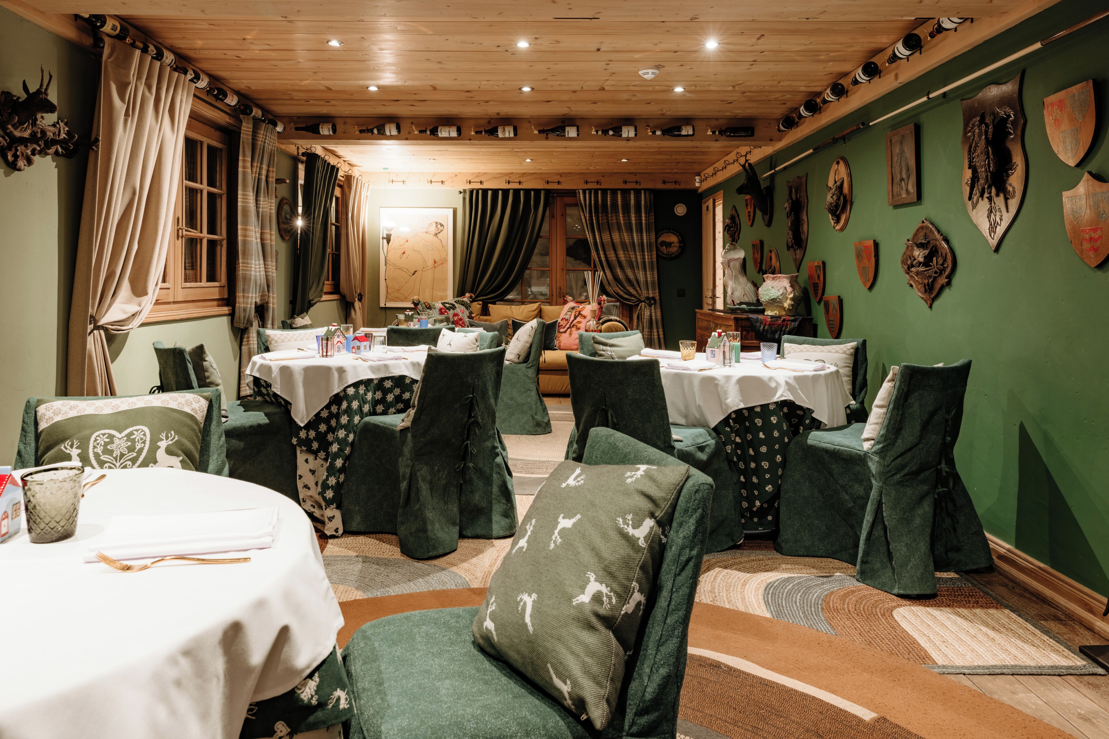 A dining area with round tables, green upholstered chairs, and a wooden ceiling.