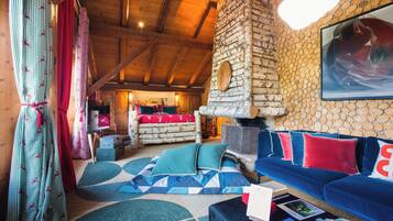 Ein gemütliches Zimmer mit einem Steinofen, einem blauen Sofa mit roten Kissen und einem gemusterten Teppich.