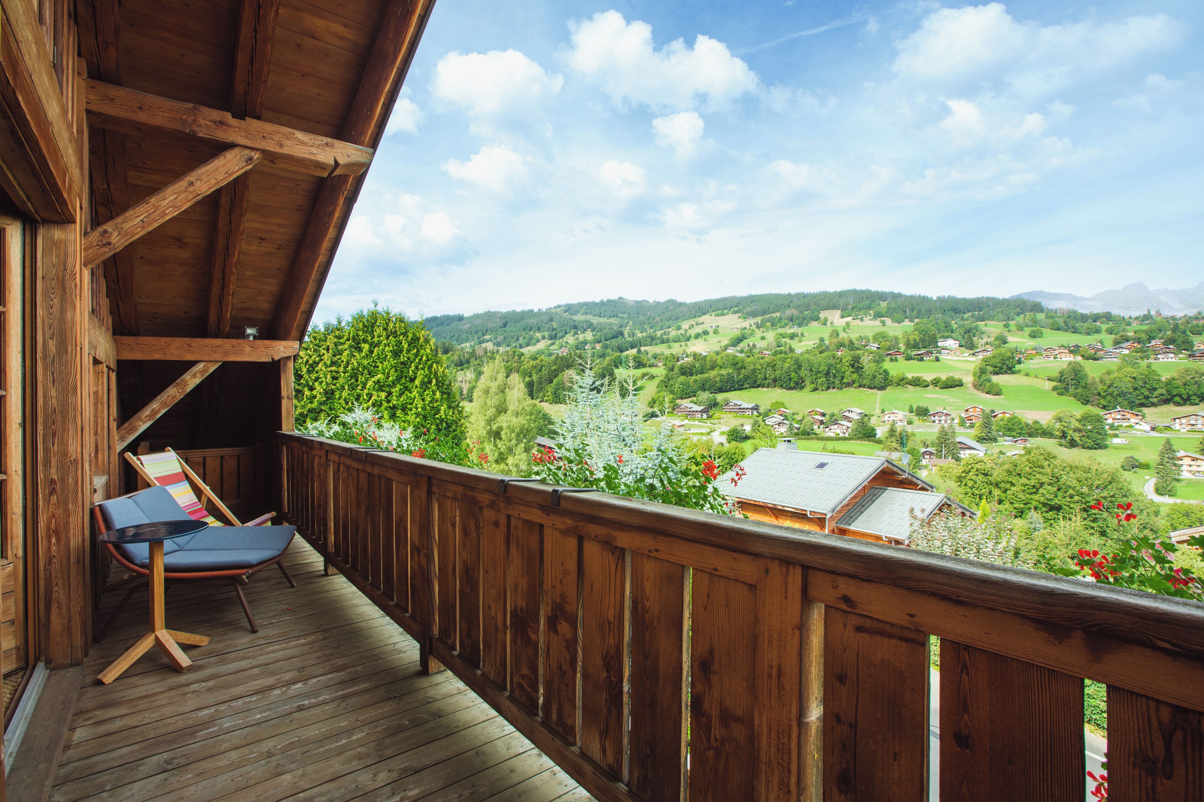 A wooden deck with a view of a green valley and houses.
