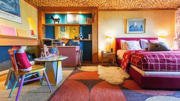 A cozy room with a bed, a desk, and a chair, featuring a unique ceiling design and a colorful rug.