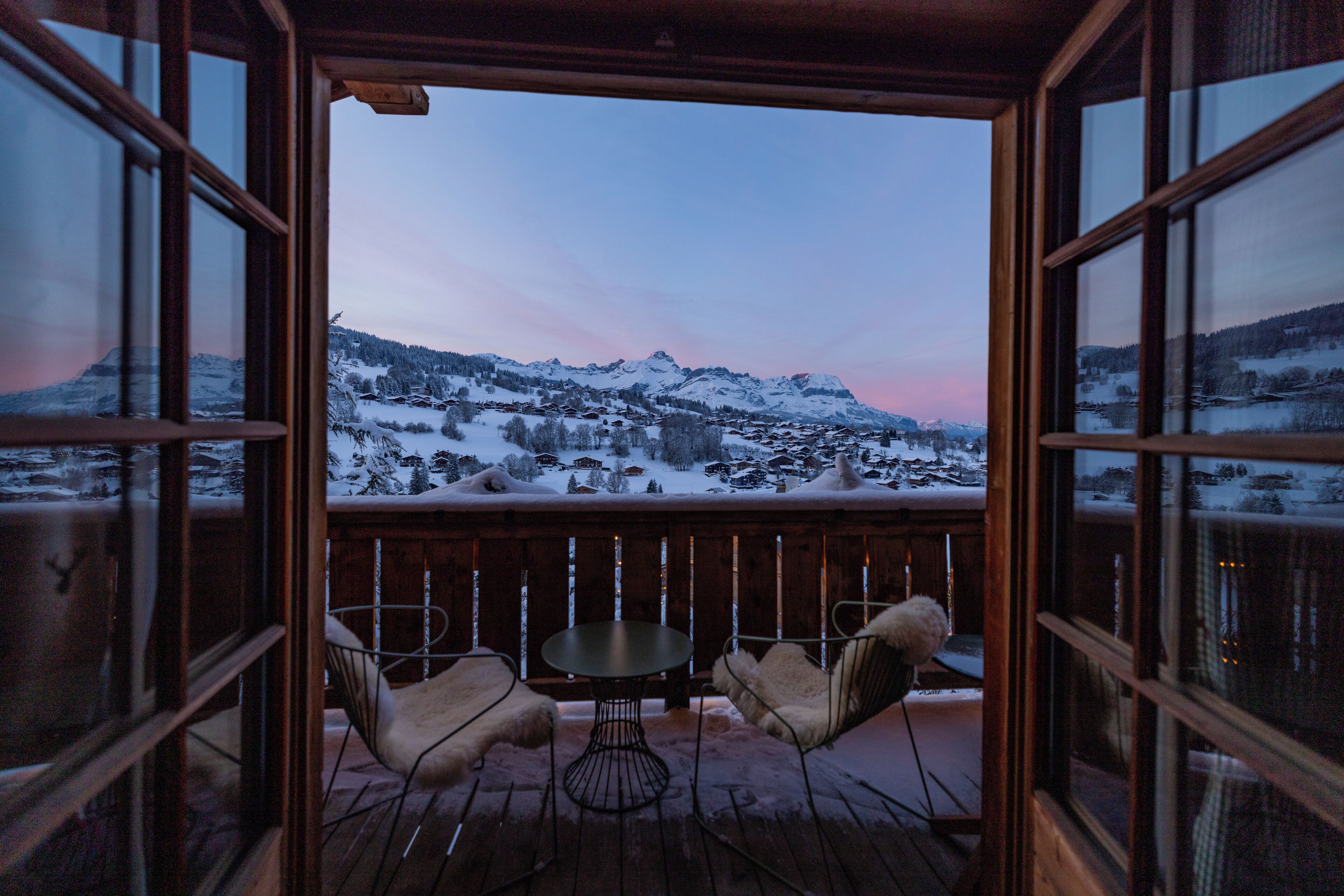 A wooden deck with a table and chairs, overlooking a snowy mountain landscape.