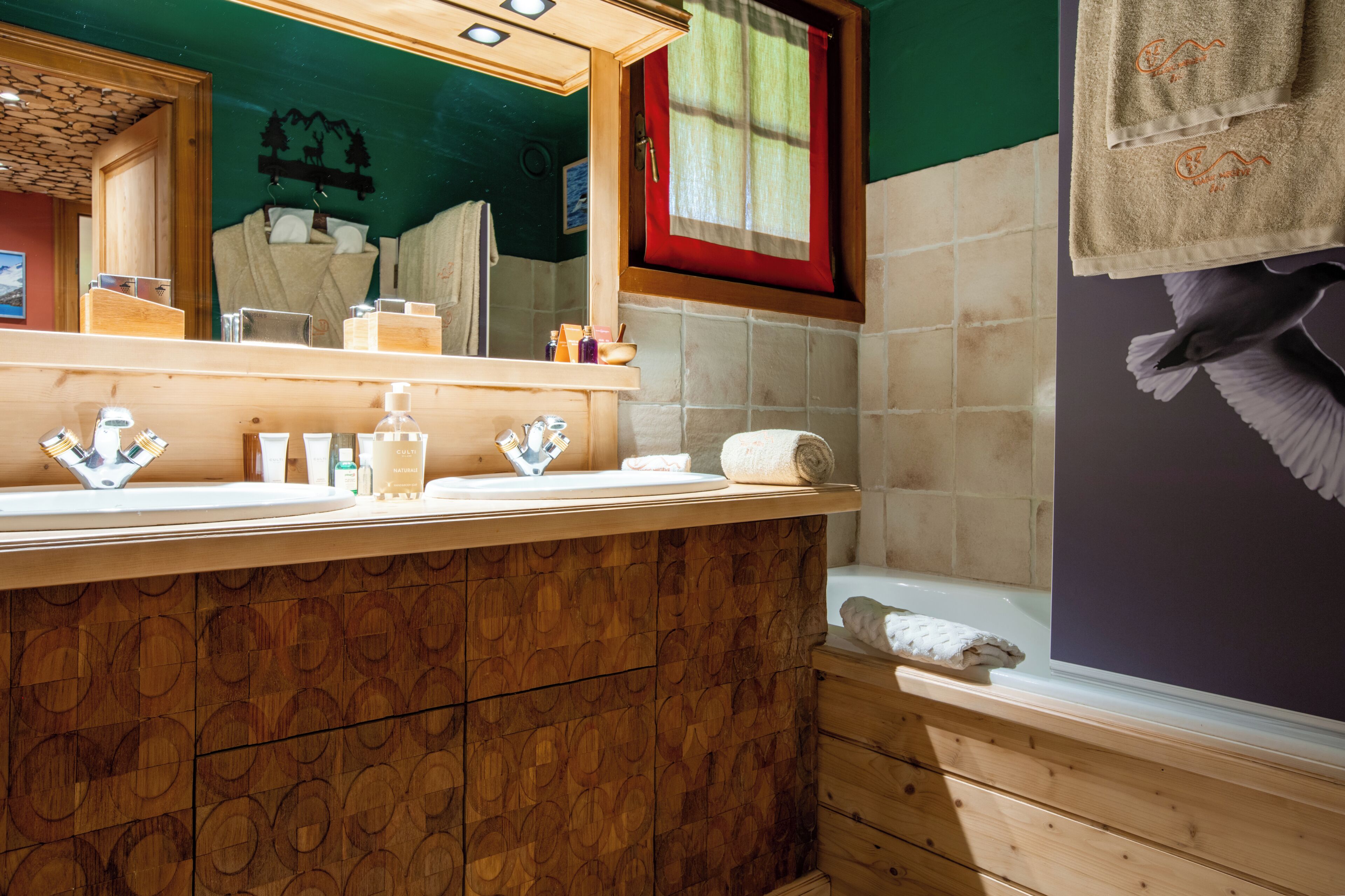 Un bagno con un mobile vanitario in legno, uno specchio, una finestra con tenda rossa e un asciugamano appeso al muro.