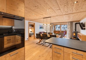 A modern kitchen with wooden cabinets, a built-in oven, and a dining area with a table and chairs.
